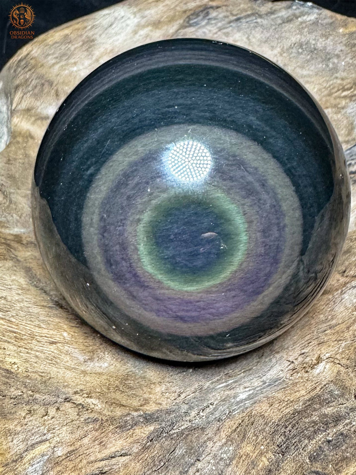 Sphère en obsidienne œil céleste du Mexique sur bois, avec un centre bleu décalé vers le bas et des anneaux jaune-vert et violets.