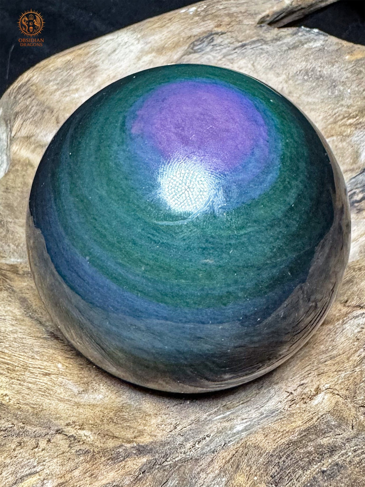 Obsidienne Manta Huichol taillée en sphère, avec une grande plage violette en partie haute et des bandes bleues sur fond vert profond.