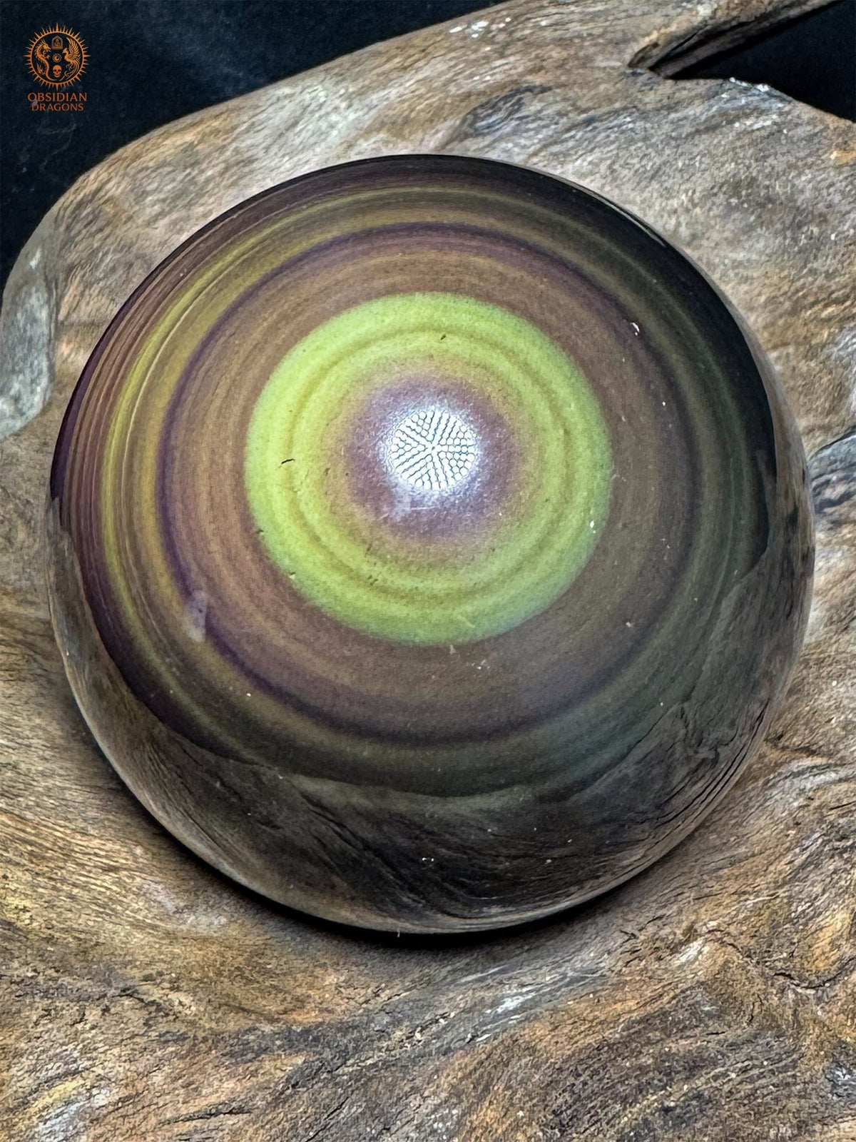 Sphère en obsidienne œil céleste du Mexique de 7 cm, avec un anneau jaune-vert entourant un centre violet, posée sur du bois - Obsidian Dragons