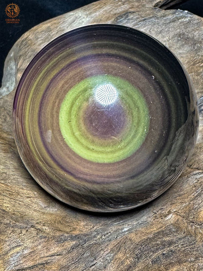 Gros plan de la sphère en obsidienne œil céleste : large anneau jaune-vert autour d’un centre mauve et bandes concentriques bronze et violettes