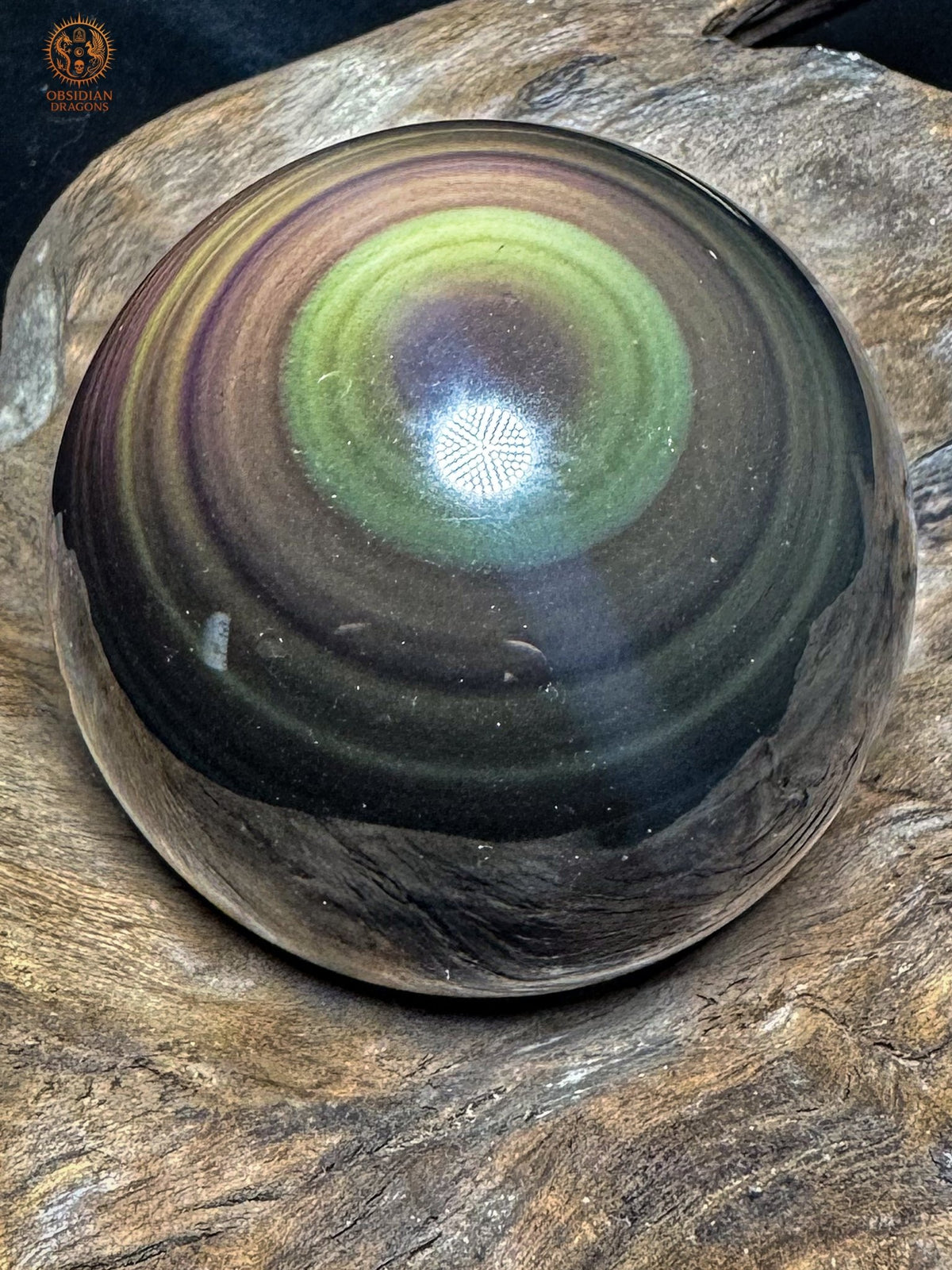 Sphère en obsidienne œil céleste vue inclinée sur du bois, avec un anneau jaune-vert dans sa partie supérieure et un centre violet