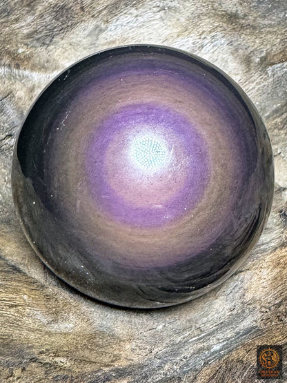 Sphère en obsidienne œil céleste aux reflets violets, cœur mauve rosé et anneau violet soutenu, posée sur bois - Obsidian Dragons