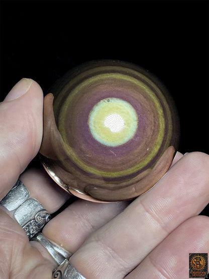 Sphère en obsidienne œil céleste de 5,25 cm tenue en main, centre jaune-vert et couronnes mauves, violettes et vertes - Obsidian Dragons