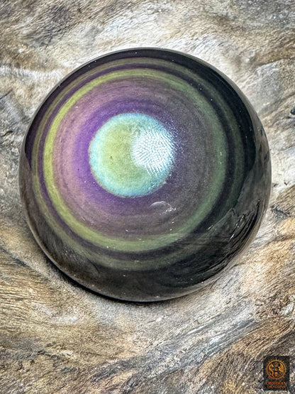 Sphère en obsidienne œil céleste vue légèrement de biais, centre vert clair bordé de bleu cyan et anneaux violets et mauves.