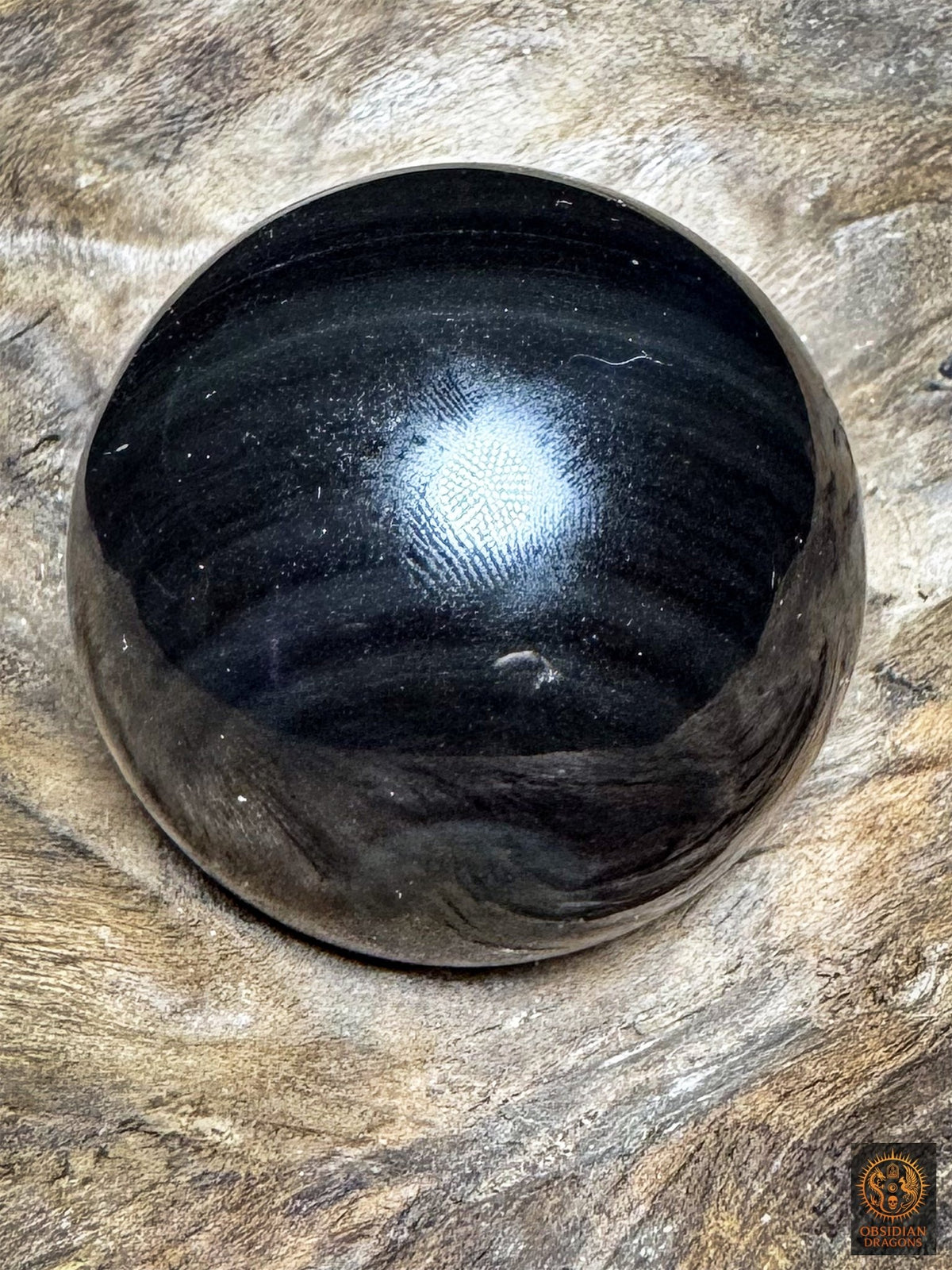 Face sombre de la sphère en obsidienne œil céleste, surface noire polie parcourue de discrètes bandes gris-bleu.