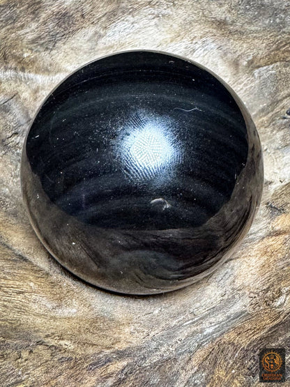 Face sombre de la sphère en obsidienne œil céleste, surface noire polie parcourue de discrètes bandes gris-bleu.