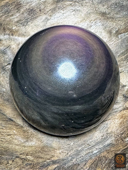 Vue inclinée de la sphère en obsidienne, couronne violette en partie haute et bandes gris-vert sur les zones sombres.