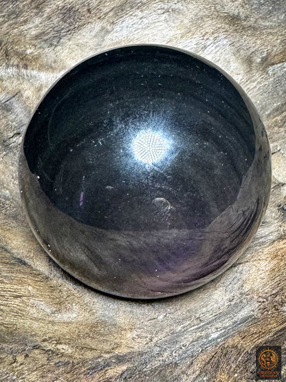 Vue latérale de la sphère en obsidienne polie, avec de discrets reflets violets et des bandes gris-vert sur fond noir.