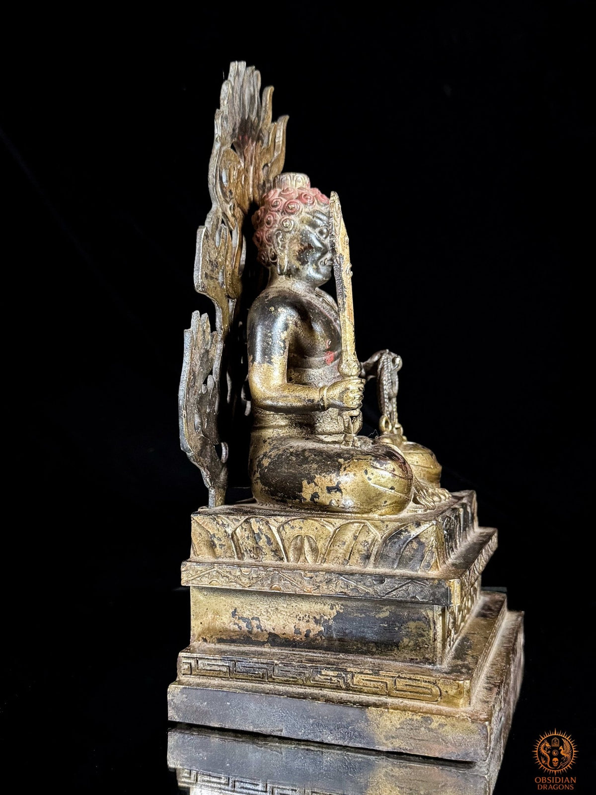 Vue latérale côté épée de la statue d’Acala en bronze, montrant la posture du lotus, le socle architectural et la mandorle ajourée.