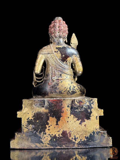 Vue arrière de la statue d’Acala en bronze montrant le vêtement sculpté, le socle massif et la patine noire, dorée et rouge.