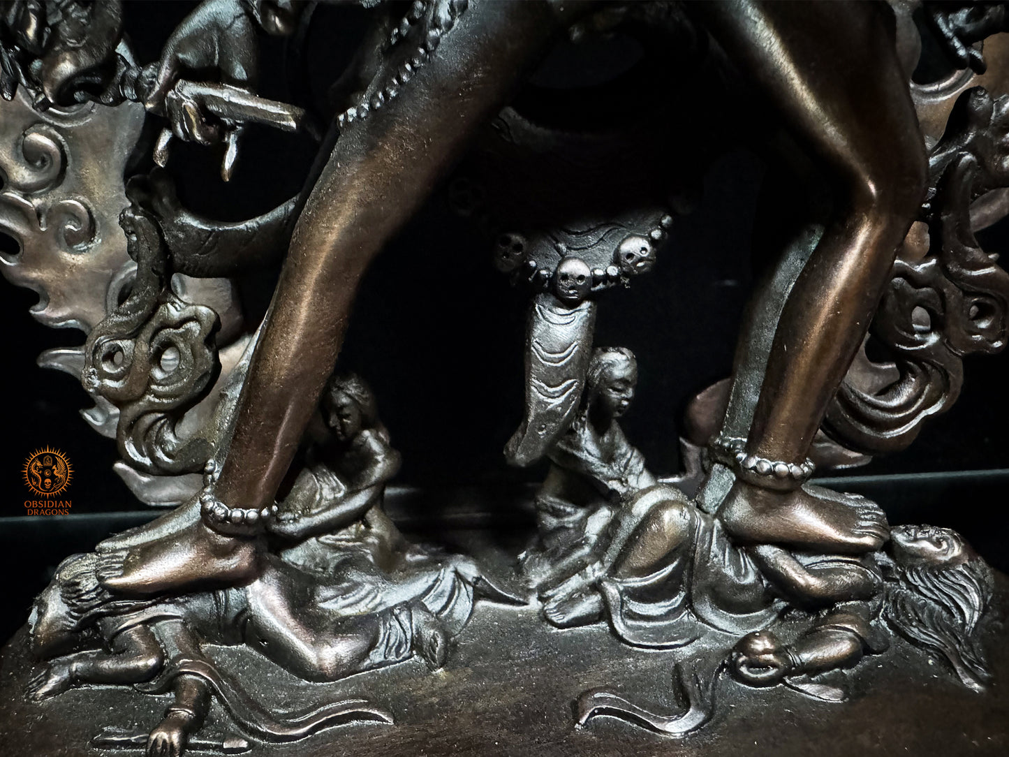Détail du socle de la statue de Kalachakra en bronze, avec pieds ornés, figures foulées et symboles de victoire sur les obstacles

