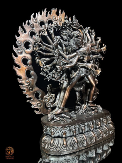 Vue de trois quarts gauche de la statue de Kalachakra en bronze violet révélant la profondeur des bras, attributs et flammes ajourées
