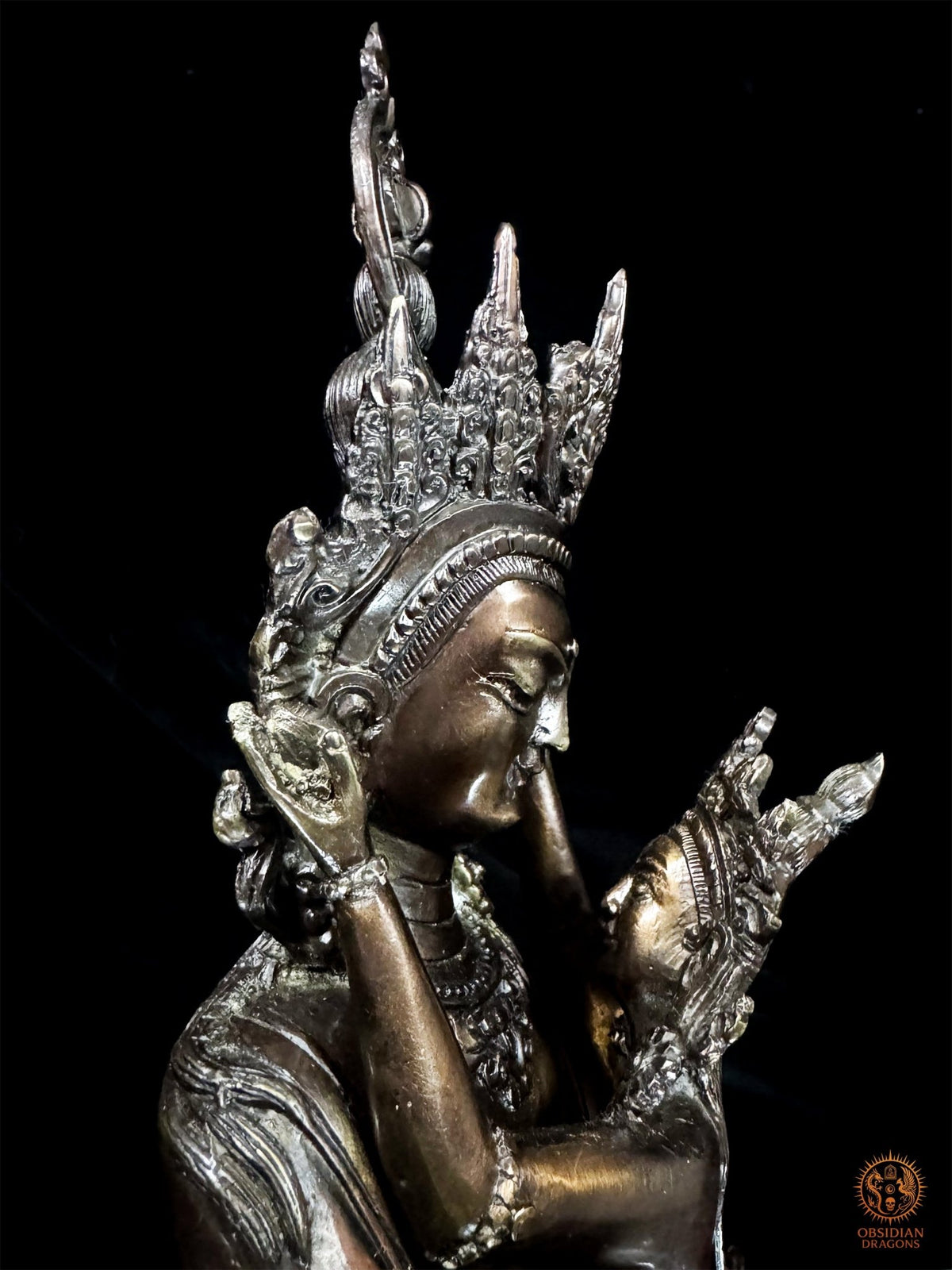 Gros plan de profil sur les visages rapprochés de Vajrasattva et de sa parèdre en bronze, leurs couronnes et leurs parures.