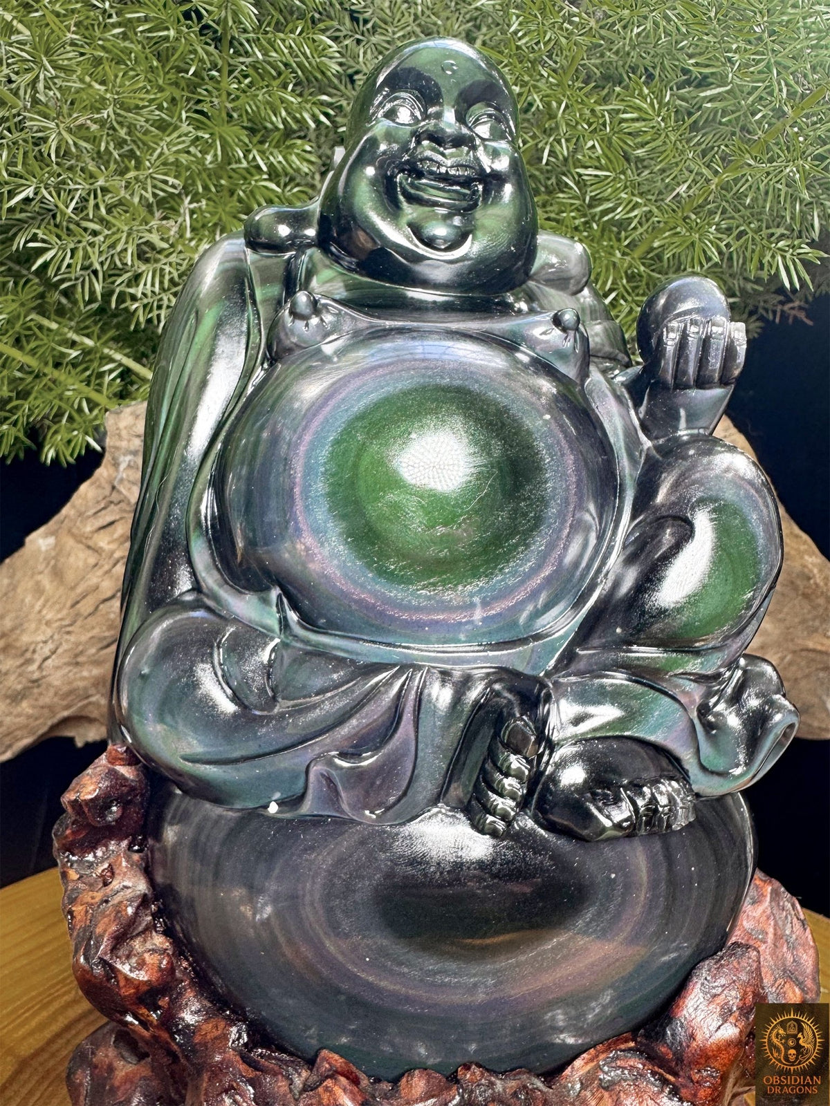 Vue rapprochée du Bouddha rieur en obsidienne œil céleste sur son support en cèdre, avec des anneaux irisés sur le ventre et le sac.