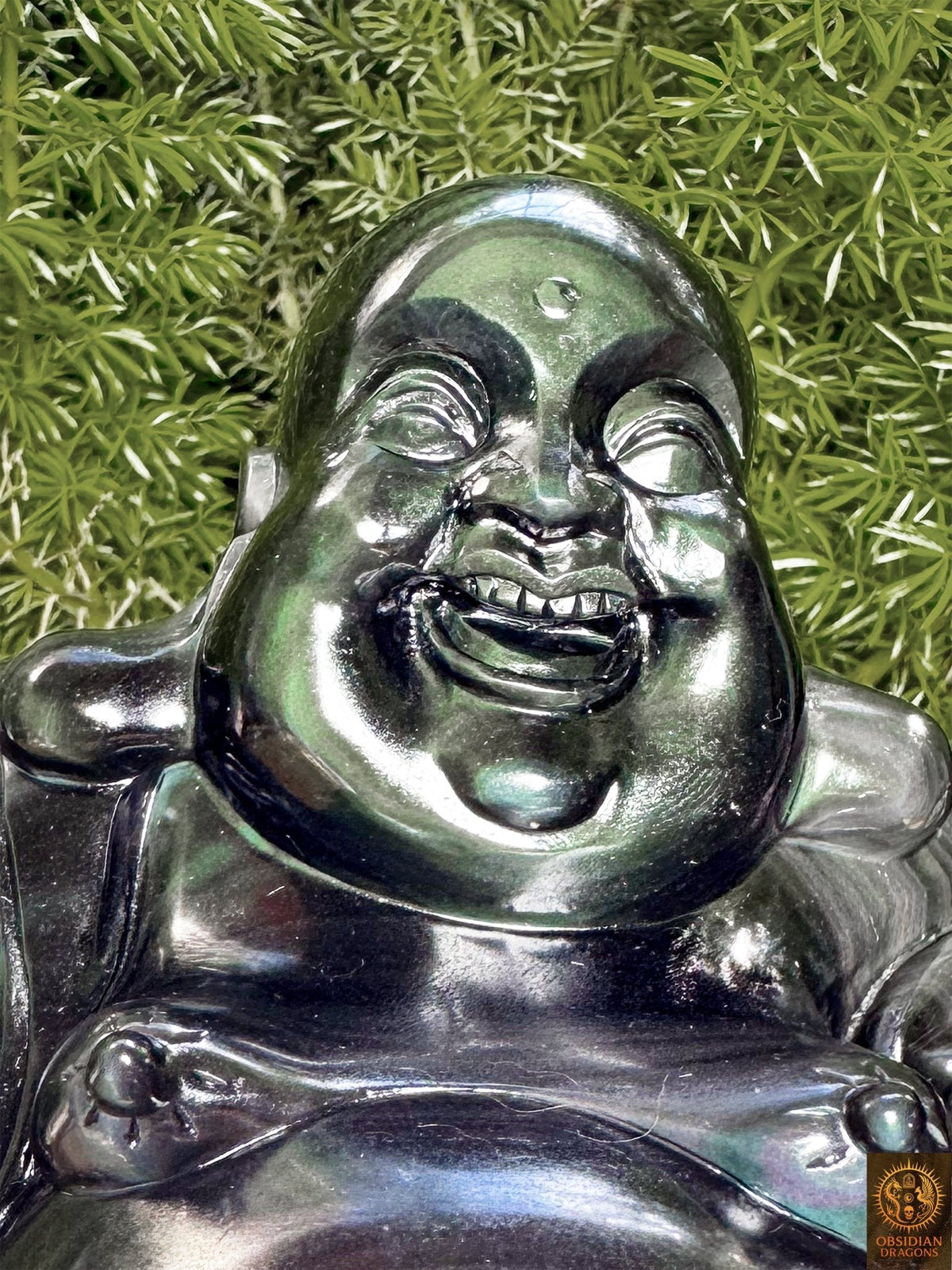 Gros plan du visage souriant de Budai, Bouddha rieur sculpté en obsidienne œil céleste aux reflets verts et argentés.