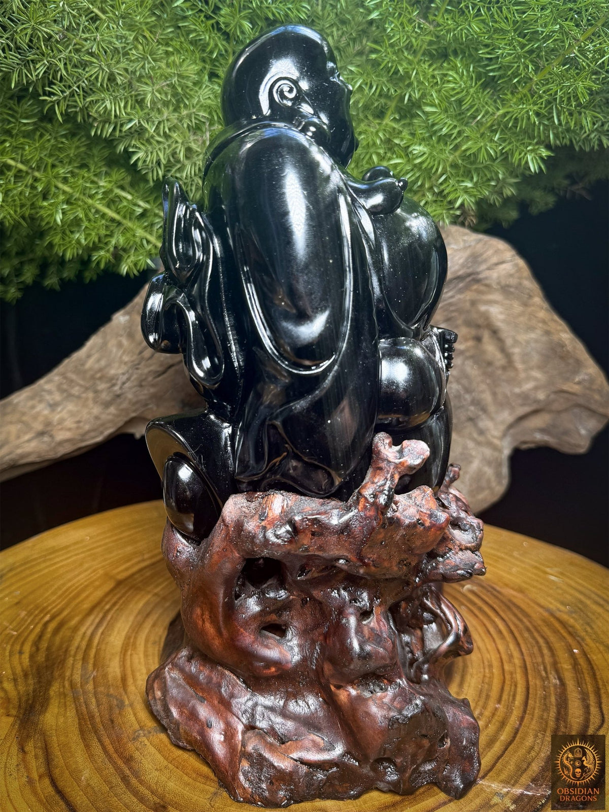 Profil de Budai tourné vers la droite sur son support en cèdre, montrant le ventre arrondi et le vêtement sculpté en obsidienne œil céleste.