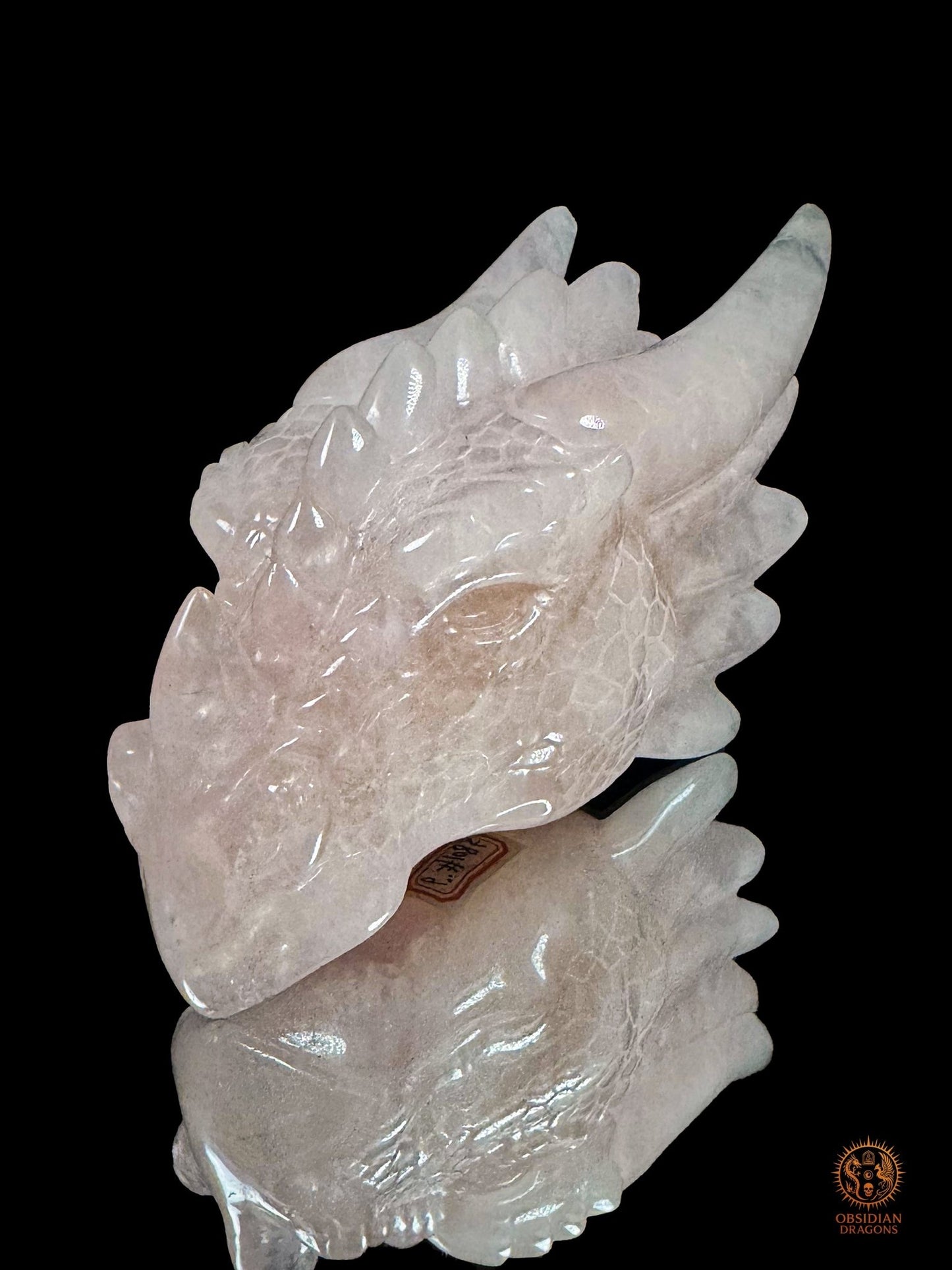 Gros plan de la tête de dragon en quartz rose naturel, montrant le profil du museau, l’œil, les écailles et le poli brillant de la sculpture
